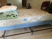 Twin mattress, box spring and expandable metal frame displayed with pillow and blankets on top