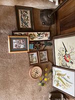 Framed wall decor collection including a large bird print, botanical prints, a clock, needlepoint, and metal leaf wall art arranged on carpet.