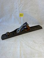Side angle view of the Stanley No.7 wood plane to show overall length, metal body, and wooden handles.
