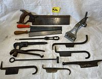 Full view of lot including saws, wrench, clamps, pliers, and various hook tools on white cloth
