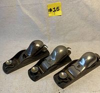 Three Stanley knuckle cap block planes with shiny metal knuckle caps displayed on a neutral cloth background, showing overall condition and markings.