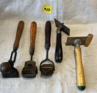 Five antique hand scrapers with wooden handles arranged side by side showing overall condition and variety in blade shapes and handle colors.