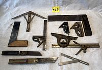 Overview of all antique and vintage hand tools laid out on a white cloth showing various squares, bevel gauges, and measuring tools with patina and wear.