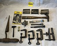 Photo showing the entire lot of vintage and antique hand tools arranged on a white cloth including clamps, handles, hammers, nuts, and a Stanley booklet.