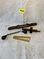 Photo showing all four vintage woodworking tools on a beige fabric background: spokeshave, folding ruler, drawknife, and marking gauge.