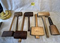Full view of 6 wooden mallets and a yellow curved object, showing variety in shape, size, and wood tone.