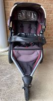 Front-facing view of the jogging stroller showing padded seat, child tray with cup holders, canopy with window, and front swivel wheel.