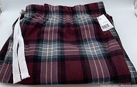Folded pair of men's plaid pyjama pants with visible white drawstring and burgundy dominant color