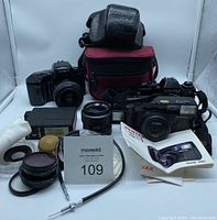 Overview photo showing Minolta Maxxum 5xi with lens, Pentax Zoom 70-S camera with manual, Contax camera in leather case, Bell & Howell flash unit, extra lenses, and camera bags.