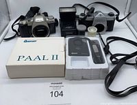 Wide view showing the lot contents: Pentax MZ-50 and Asahi Pentax SP1000 cameras, Focal M500T-Zoom flash, Quorum Paal II alarm in packaging, and small roll of film, all on white backdrop.