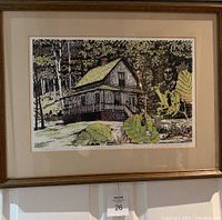 Framed and matted silkscreen print of a pioneer home set in a wooded area, showing the full front view of the art piece hanging on a wall.