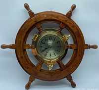 Front view of a wooden ship wheel clock with visible brass bezel and clear clock face showing time and 'Ship's Time' text.