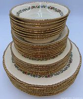 Stacked 32-piece set with visible gold trim and floral decoration on edges of plates and bowls.