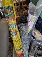 Four rolls of various wire fencing including chicken wire and garden mesh rolls organized upright against a chair.