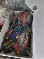 Box filled with five multicolored metal fish wall decorations featuring detailed scales and segmented fins.