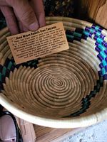 Basket showing intricate coiled weaving and colored bands inside rim with a hand holding a card describing the basket as handmade in Tanzania