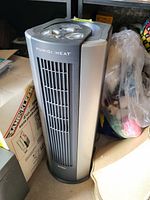 Humidi Heat tower heater shown from front angle with control panel on top, surrounded by household items.