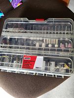 Plastic organizer case containing various hobby rotary tool accessories including drill bits, sanding drums, polishers, and brushes.