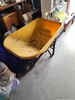 Yellow metal wheelbarrow positioned indoors on concrete floor, showing interior and tire.
