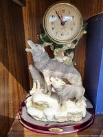 Clock with two wolf figurines on snow and tree base, mounted on maroon stand with plaque