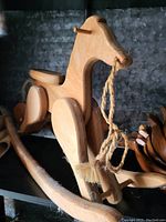 Photo of a light-colored wooden handcrafted rocking horse with a rope reins attached, showing side profile and rocker base.