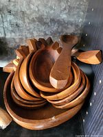 Stack of eight oval wooden bowls with two wooden spoons and one wooden scoop on top.
