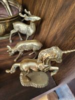 Three brass animal figurines including a reindeer, pig, and unicorn displayed on a wooden shelf