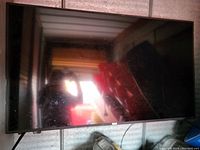 Photo of a 50 inch flat screen TV with black bezel mounted or standing, screen off showing reflection and smudges.