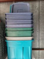 Stacked plastic totes with lids in various colors including gray, green, beige, and turquoise.