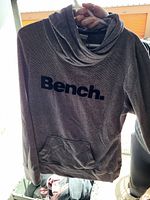 Front view of grey Bench hoodie sweater with cowl neck, black printed logo, and front pocket.