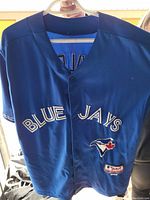 Front of blue Toronto Blue Jays baseball jersey with button front, 'BLUE JAYS' text and logo patch.