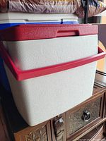 Side view of the cooler showing textured white body with red lid and carrying handle.