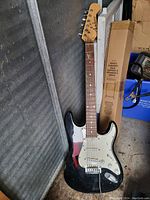 Black Richmond electric guitar leaning against a wall, showing full guitar body, neck, headstock with the brand name, and parts of the room surroundings.