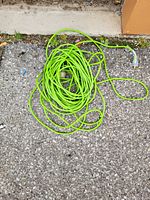 Photo of a long green extension cord coiled on the ground showing both plug and socket ends.