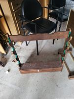 Wooden firearm rack showing vertical slots with green padding for holding firearms, base storage drawer, and overall condition.
