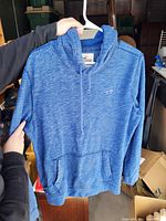 Front view of blue Hollister pullover sweater hung on a white hanger showing the full front and pocket detail.