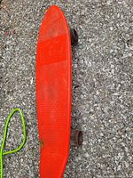 Top view of red hot dog style skateboard on asphalt surface showing elongated narrow deck with textured grip and wheels.