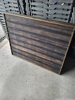 Photo of dark stained wooden panel with horizontal slats, leaning against stacked plastic crates