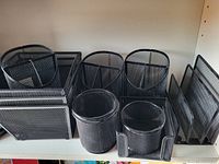 Nine black metal mesh desk organizers including cylindrical pen holders and horizontal paper trays