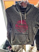 Front view of grey Roots hoodie sweater with red logo on chest, hanging on hanger.