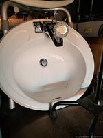 Downward view of a round white ceramic sink with a metal faucet and a visible drain with stopper.
