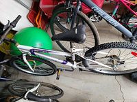 White Supercycle mountain bike with purple accents, black seat, and knobby tires, photographed indoors leaning against other bikes.