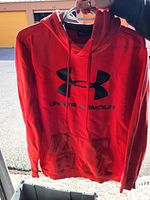 Front view of red Under Armour hoodie sweatshirt showing black logo and text.