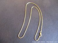 Full view of braided gold chain necklace laid flat against black background