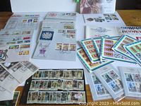 Wide view showing multiple first day covers depicting Queen Elizabeth, stamp sheets, and albums spread on table.