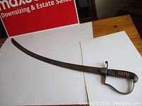 Full view of curved single-edged sword with metal guard and grooved wood handle showing surface oxidation.