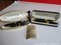Two open pen cases (white and brown) with writing instruments and instruction booklet