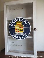 Front view of vintage wooden and glass lockable key cabinet featuring metal Cadillac Authorized Service sign on front glass and internal key hooks.