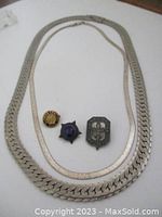 Full view of two sterling silver chains laid flat, three pins including a 1960's Scouts badge and an antique typist pin arranged on a white surface.