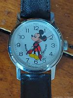 Close-up image of the watch face showing Mickey Mouse figure with red-gloved rotating hands and clear numerals.